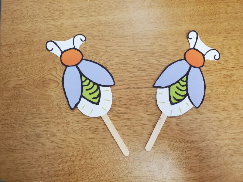 Two paper fireflies attached to popsicle sticks.