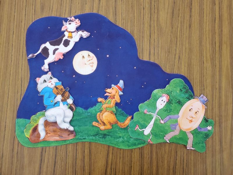 Professionally printed flannel with pieces of the cat and the fiddle, the laughing dog, a cow, and the dish and spoon, with a background piece with green grass and a night sky featuring a full moon with a face for the rhyme "Hey, Diddle, Diddle"