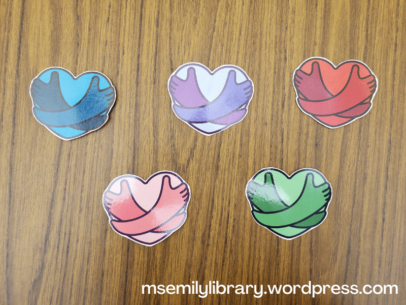 Five printed and laminated icons of hearts with arms embracing them in blue, purple, red, pink, and green.