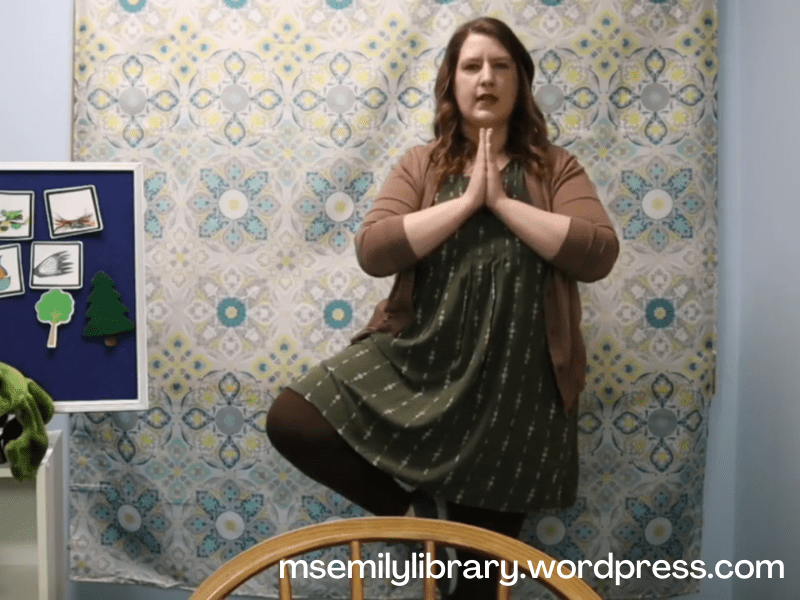 Screenshot from virtual storytime video, showing Ms. Emily in Tree Pose.