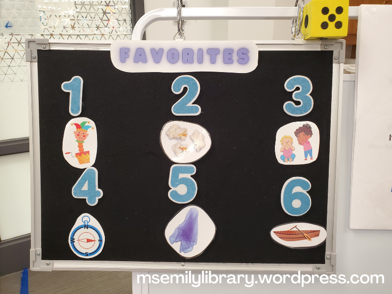 Flannelboard marked "Favorites" at the top, then numbered 1-6. Icons are: 1 jack in the box 2 popcorn, 3 two kids playing peek a boo 4 compass pointing east 5 purple scarf 6 a boat with oars