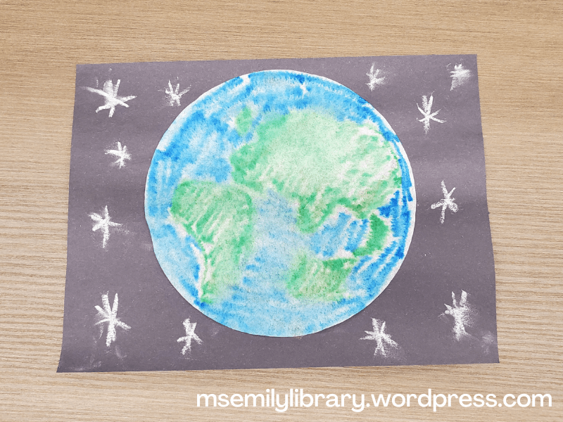 Craft showing a blurry blue and green earth glued to a piece of black construction paper. White chalk stars were drawn around the earth.