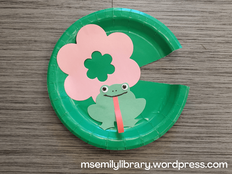 craft with a green plate with a small wedge cut out, decorated with a pink paper flower and frog with googly eyes and a long curly strip of red paper for a tongue.