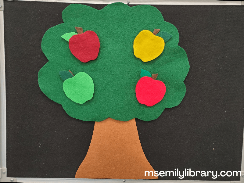 Flannel showing a large simple tree with green foliage and four large apples of different colors: dark red, yellow, light green, and light red.