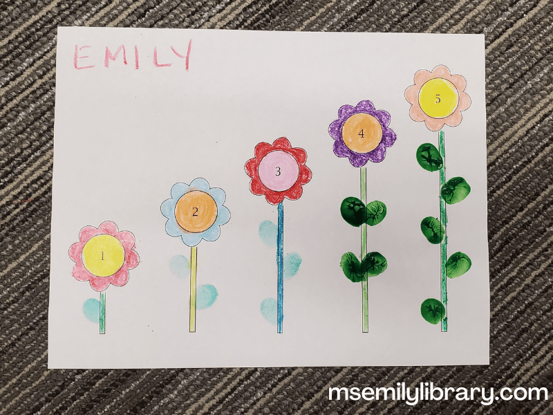 craft showing five flowers with increasingly tall stems. In the center of each flower is a number, 1-5 (with the tallest stem showing 5). The flowers are colored with crayons and each stem has a fingerprinted number of leaves corresponding with the number on the flower. The first three are pale green (stamp pad), the last two are a much darker green (fingerpaint)