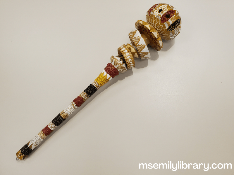 a decorative molinillo, painted with different patterns in black, white, mustard, and rust colors.