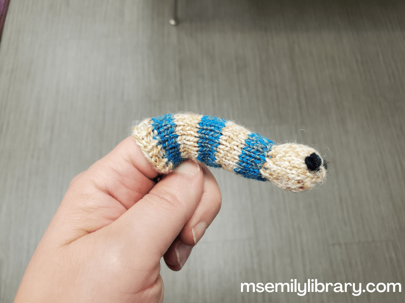 photograph of knitted worm finger puppet that is blue and beige stripes with large black eyes.