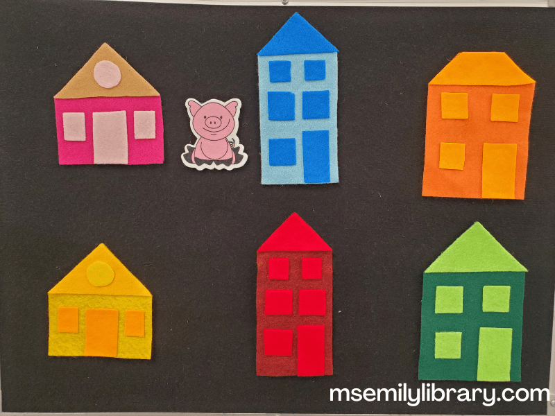 Little pig in a house flannel, showing six multi-toned houses and a pink pig. Houses are single story pink and yellow, two story orange and green, and three story blue and red.