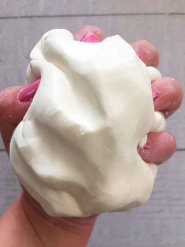 photo of a hand gripping cloud dough, a white fluffy play-dough-like material.