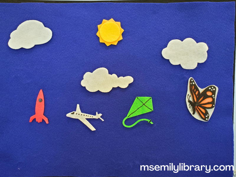 flannel of fluffy cloud what do you see, with three white clouds, an orange and black butterfly, a green kite, white airplane, red rocket ship, and yellow sun.