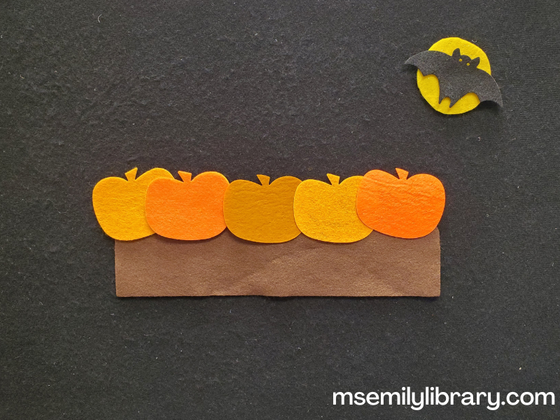 five little pumpkins flannel pieces, with a brown rectangle topped with five pumpkins of varying orange hues. in the upper right is a full yellow moon with a black bat flying across it.