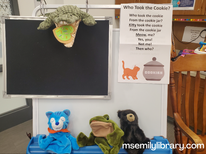 Storytime easel showing the rhyme sheet for Who took the Cookie as well as a cat, frog, and bear puppet along the bottom, and an alligator puppet with a felt sugar cookie in its mouth at the top.