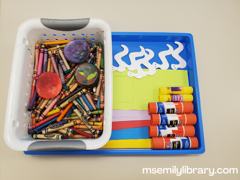 craft setup for worm craft, showing die cut worms, die cut papers with flaps in several colors, glue sticks and crayons.