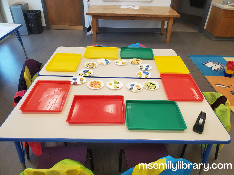 animal paw print art station table, with 8 messy trays and small plates with paint and sponges in the shape of different animal prints. there are art smocks on the chairs.