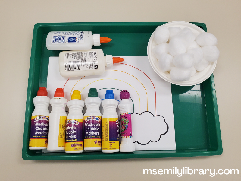 craft set up, showing a rainbow coloring sheet with cotton balls, rainbow dot markers, and liquid glue