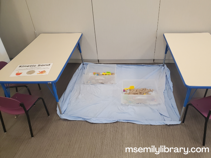 Kinetic sand station, with two bins on top of a fitted sheet held down by two tables.
