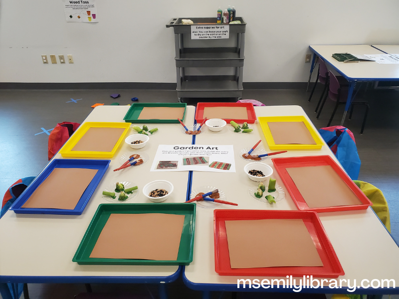 garden art station, with messy trays with brown construction paper, plates with paint, brussels sprouts and celery, and bowls with dried beans.