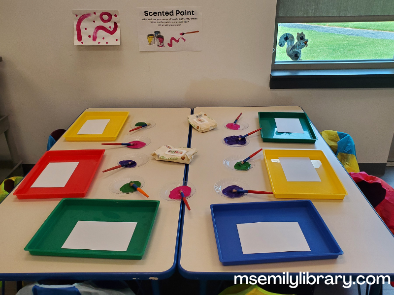 scented paint station, with messy trays with blank paper, and small plates with three colors of paint and brushes.