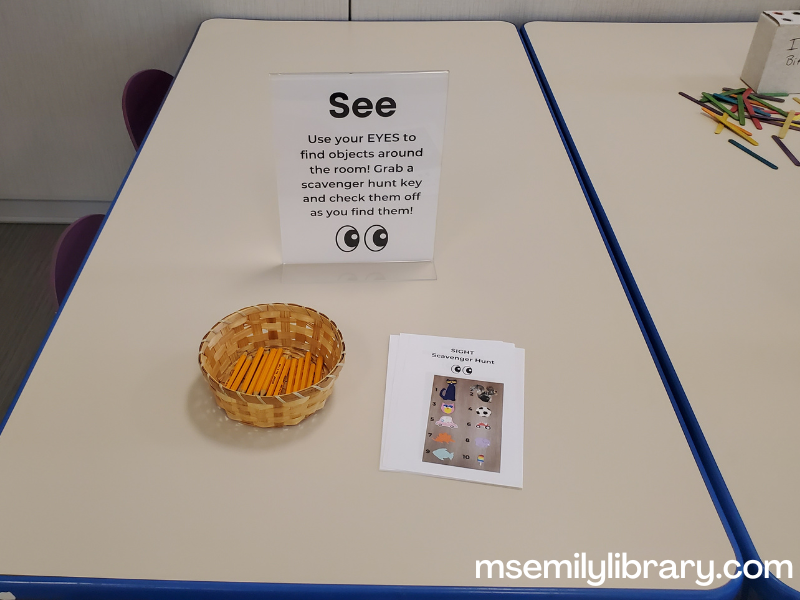 See station - showing a sign explaining a scavenger hunt, a basket of golf pencils, and a finding aid with a photo of each hidden image.