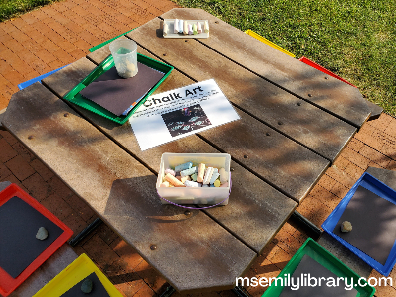art station with sidewalk chalk and black paper in messy trays
