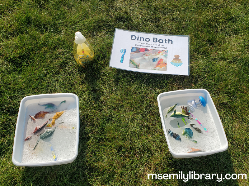 water bins with plastic dino toys, toothbrushes, dish brushes, and bubbles from baby shampoo (bottle shown off to the side)