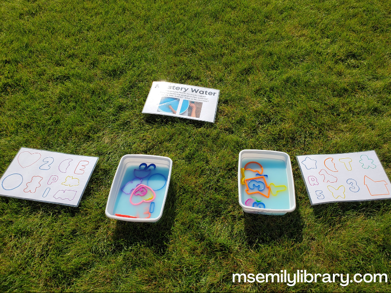 small bins with blue cloudy water and plastic cookie cutters - both bins have a "finding aid" poster with the outlines of the cookie cutters