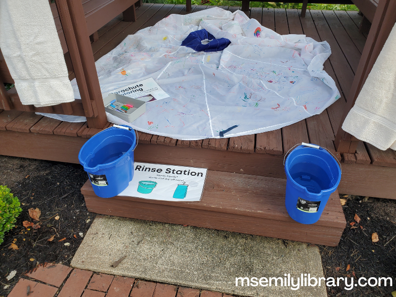 rinse station on gazebo steps, with two buckets of water and two bath towels hung over the railings (also can see the parachute inside the gazebo)