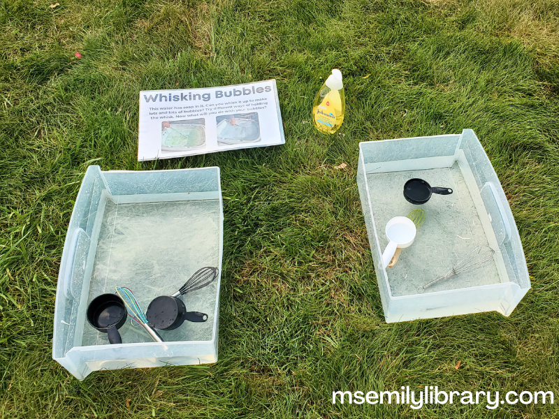 water bins with water, whisks, and measuring cups. on the lawn beside is the bottle of baby shampoo