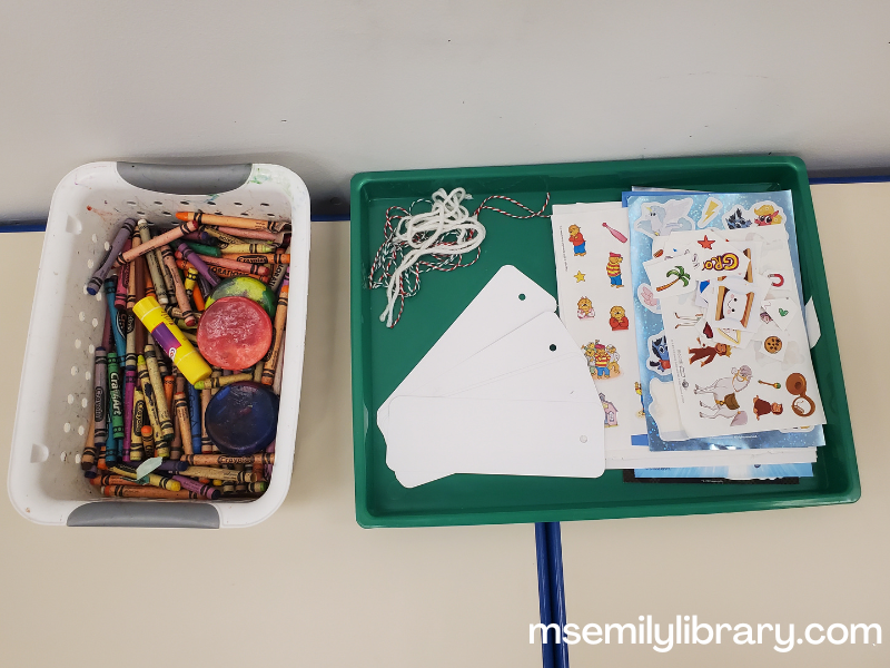 bookmark craft setup with a container of crayons, blank bookmarks, yarn, and sticker pages.